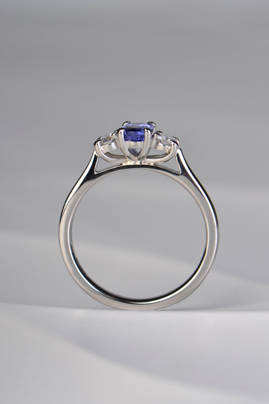 Three stone tanzanite and diamond platinum engagement ring with stones raised up so that it will sit perfcctly next to a straight wedding ring. This ring is made in the UK
