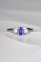 stunning oval cut intense blue tanzanite engagement ring set with two round diamonds, one on either side of the tanzanite. Each stone is held by four claws and it is made in platinum. 