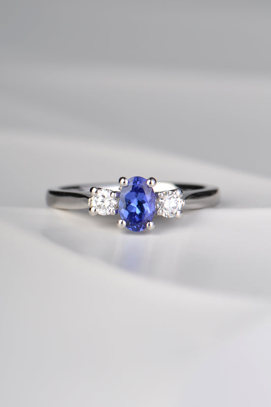 stunning oval cut intense blue tanzanite engagement ring set with two round diamonds, one on either side of the tanzanite. Each stone is held by four claws and it is made in platinum. 