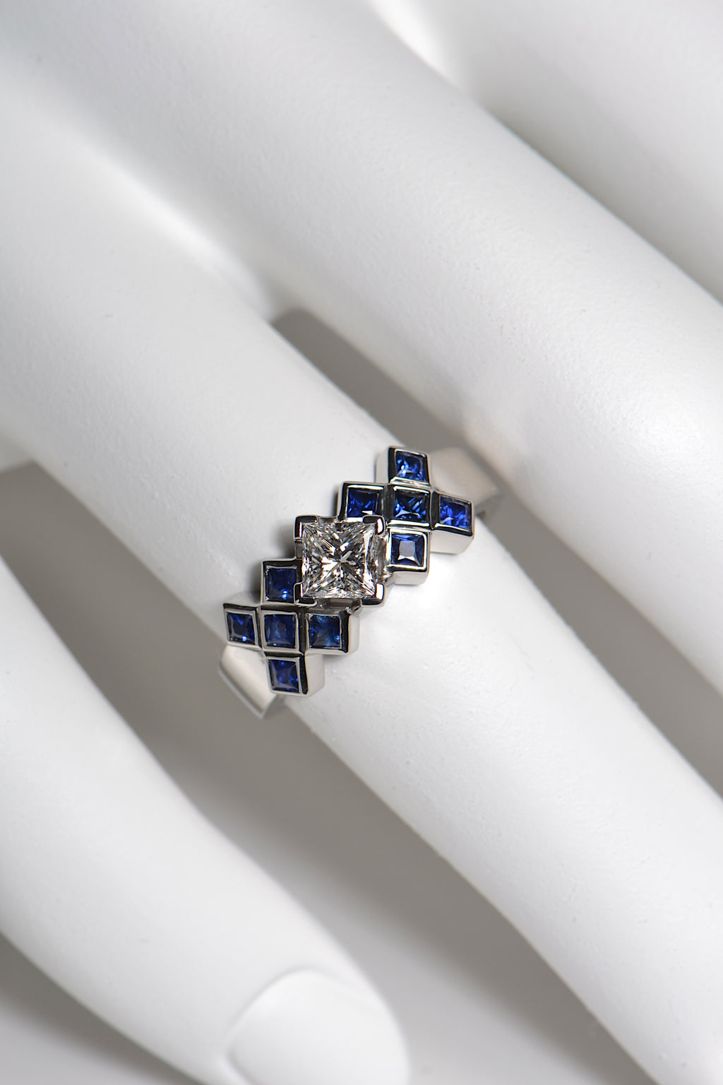The tartan ring is set with a central 0.53ct princess cut diamond above a chequered pattern of 2mm blue sapphires . The platinum ring is 7.7mm wide at the front so it is a substantial statement engagement ring. This unusual Scottish diamond ring is unmistakably scottish. 