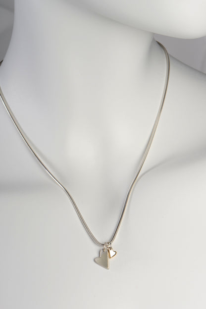 Handmade double heart necklace with large matt silver heart and small polished gold heart displayed on white mannequin to show size and scale