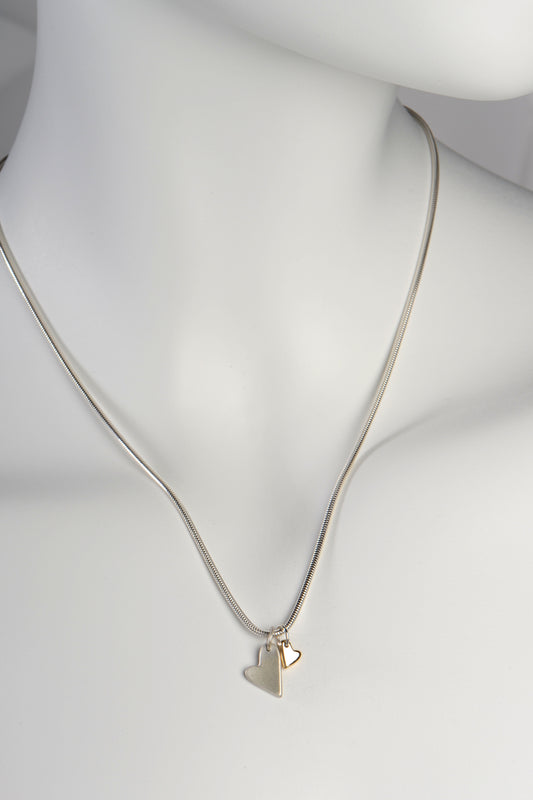 Handmade double heart necklace with large matt silver heart and small polished gold heart displayed on white mannequin to show size and scale