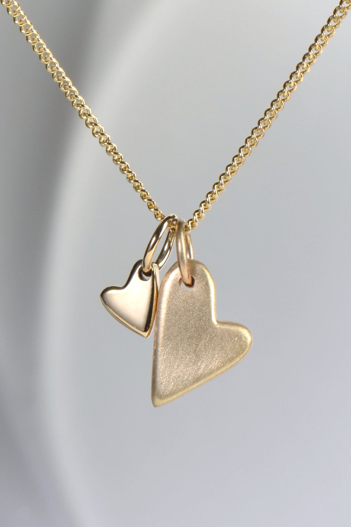 close up of 9ct yellow gold double heart necklace with brushed and polished finishes on a 45cm curb chain from the From The Heart collection by Christine Sadler