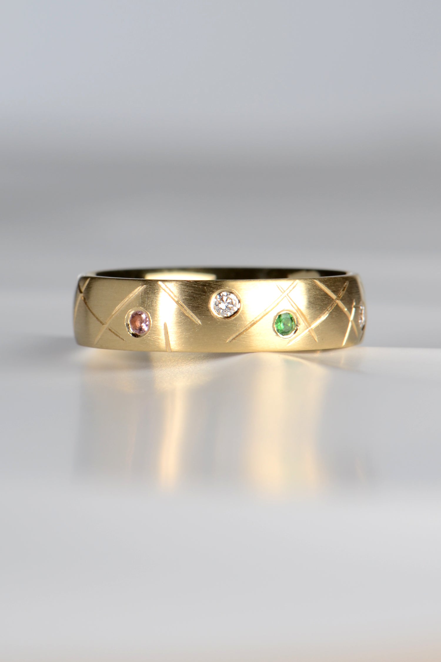 18ct gold handmade ring set with a pink tourmaline, a diamond and a green garnet with a criss cross hand engraved pattern between the gemstones. Choose your own stones and design your own ring.