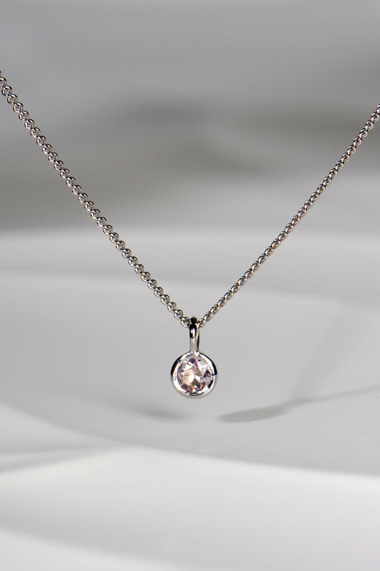 round morganite gemstone set in in round white gold pendant hanging from a curb chain