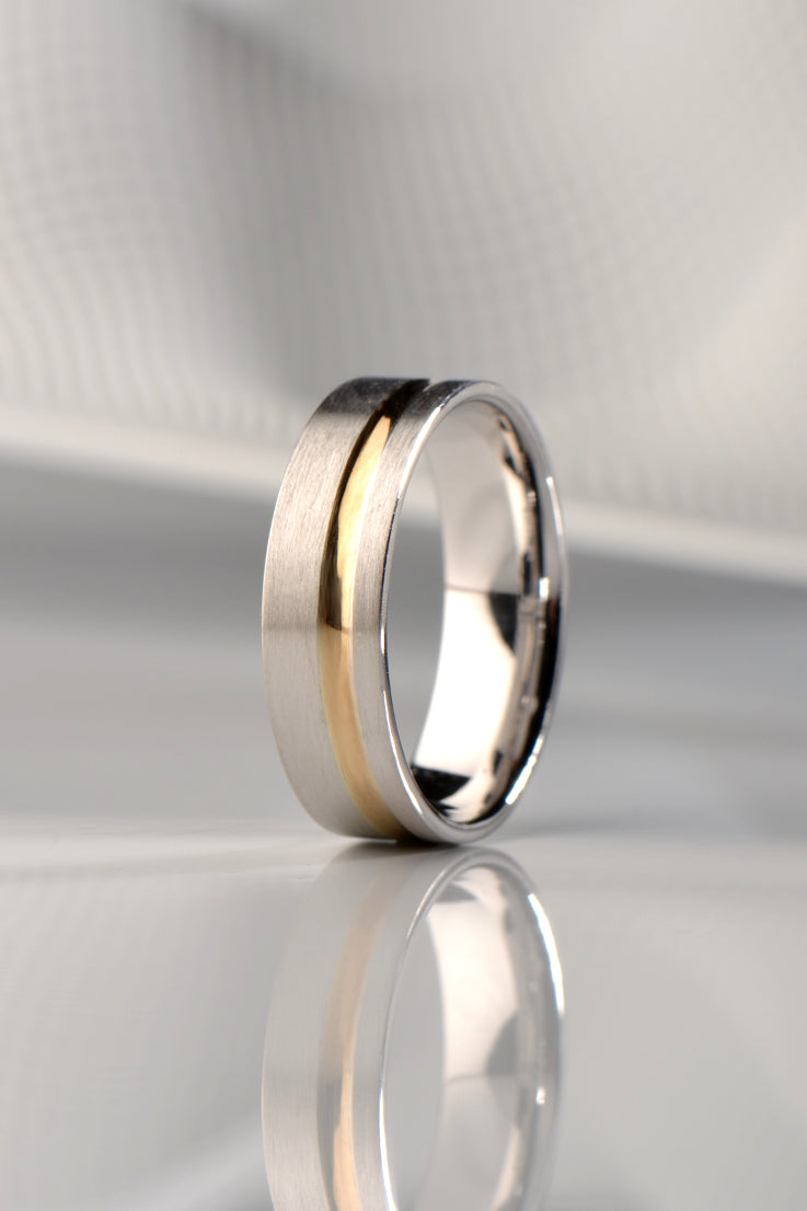 a stylish brushed white gold wedding ring for a man with a modern off set yellow gold inlay.