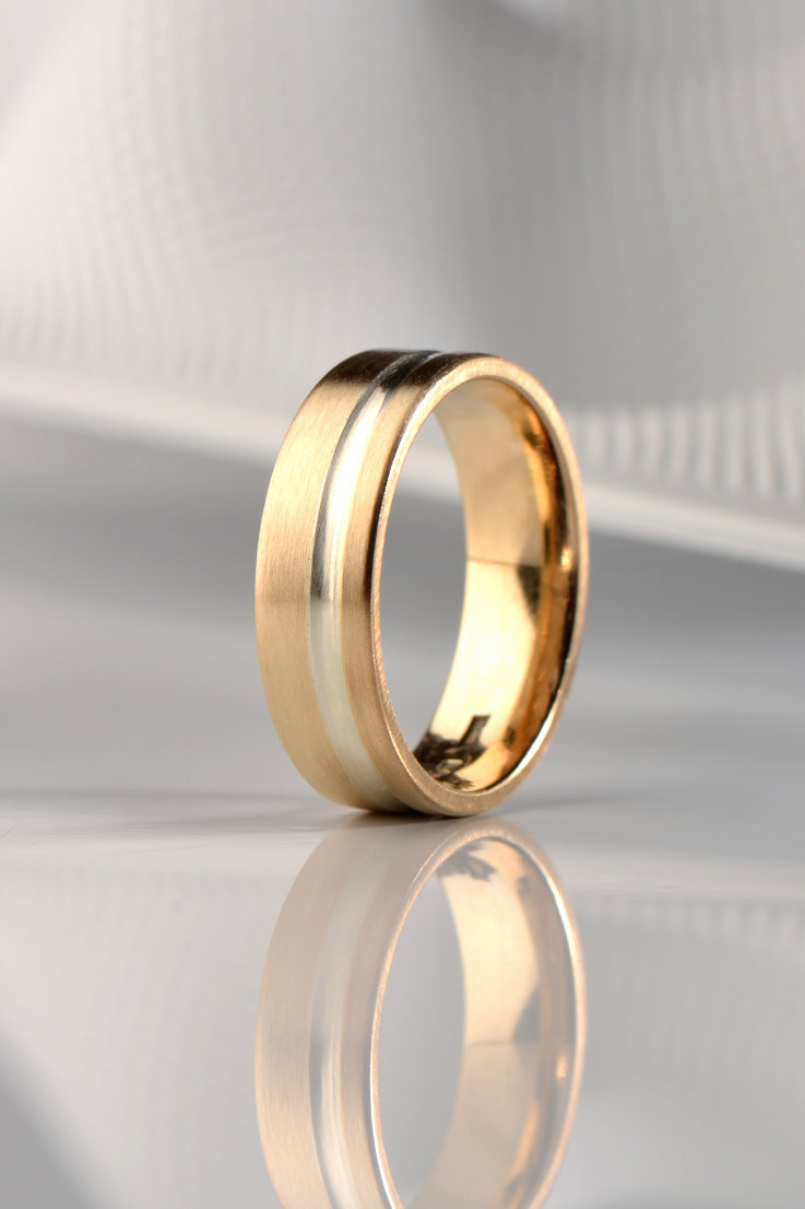 A modern brushed finished yellow gold wedding ring for a man with a white gold detail